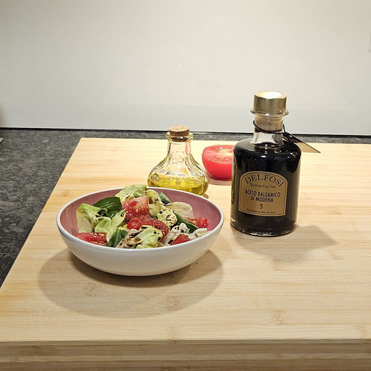 Eine Flasche Aceto Balsamico neben einer Schüssel Salat