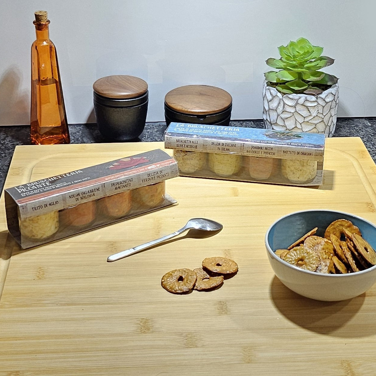 Bruschetta Creme Geschenksets auf einem Holzbrett neben einer Schale gefüllt mit Crackers