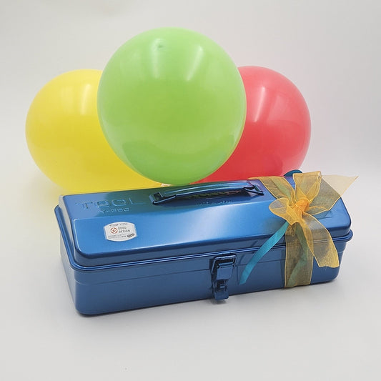 Blaue Geschenkbox mit gelber Schleife mit farbigem Luftballons im Hintergrund