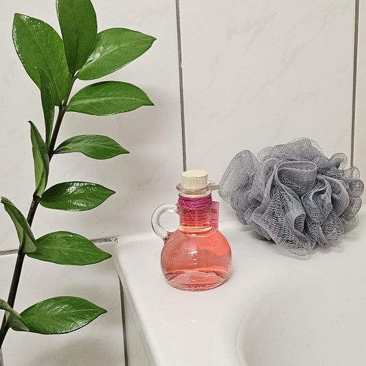 Rosenblüten-Schaumbad in dekorativem Glas am Rand der Badewanne, daneben ein grauer Duschschwamm