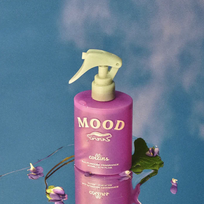 Nahaufnahme der violetten Collins Mood Water Sprühflasche mit gelbem Sprühkopf vor blauem Himmel – Alkoholfreies, kopfschmerzfreies Duftspray für Textilien und Auto.