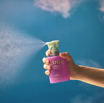 Eine Hand versprüht den feinen Nebel des Collins Mood Water French Violet Raumsprays vor blauem Himmel – Erfrischendes Textilspray für Kissen und Wohnräume.