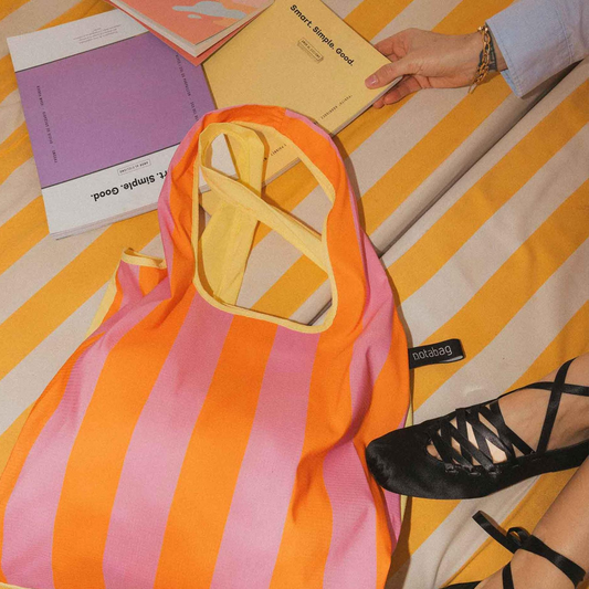 Leichte, wasserabweisende Notabag Shopper Tasche mit Pink-Orange-Gelb-Streifen, liegend am Strand