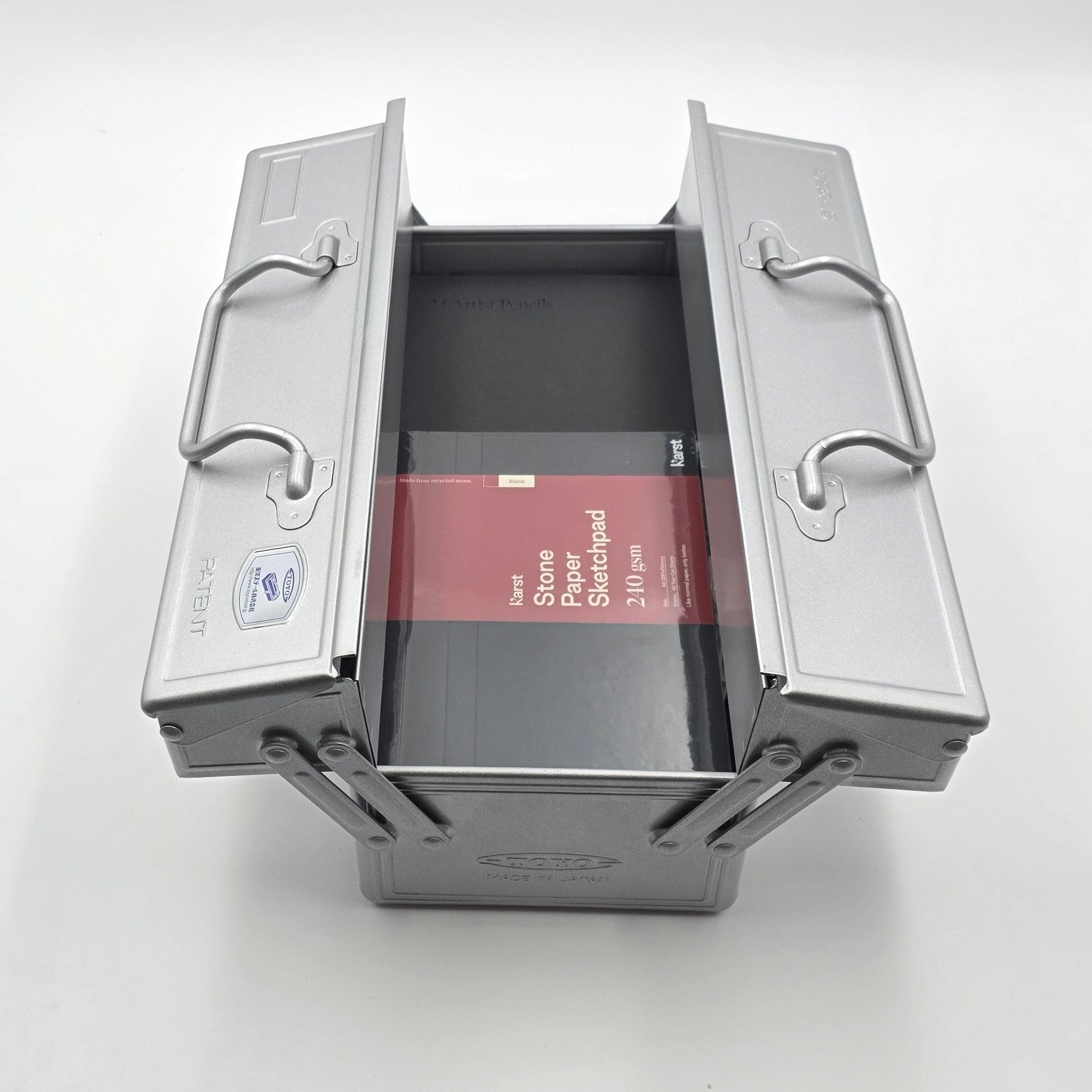 Offene Toyo Metallbox mit Skizzenblock und Farbstiften im Inneren