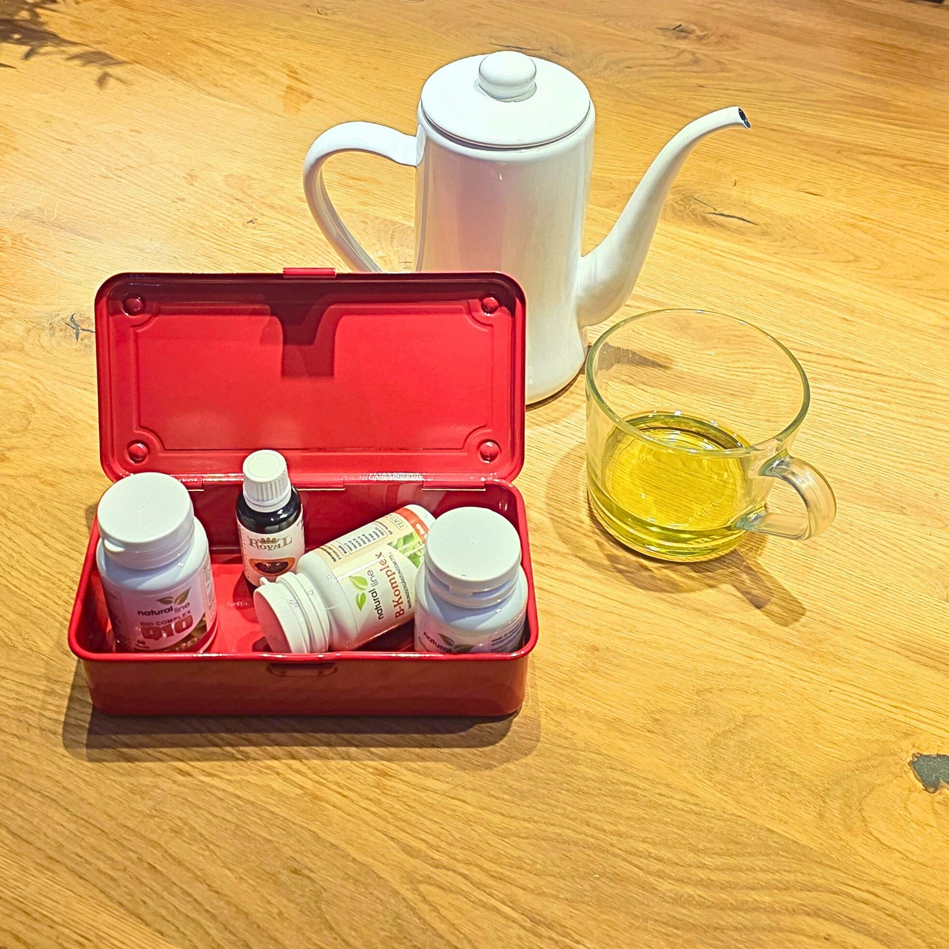 Rote Toyo T-190 Box als Aufbewahrung für Medikamente mit einer Teekanne und Teetasse im Hintergrund