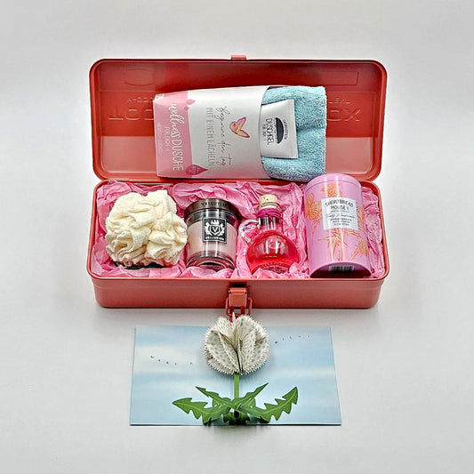 Wohlfühlzeit coralfarbene Geschenkbox mit geöffnetem Deckel, zeigt den Inhalt mit verschiedenen Produkten.
