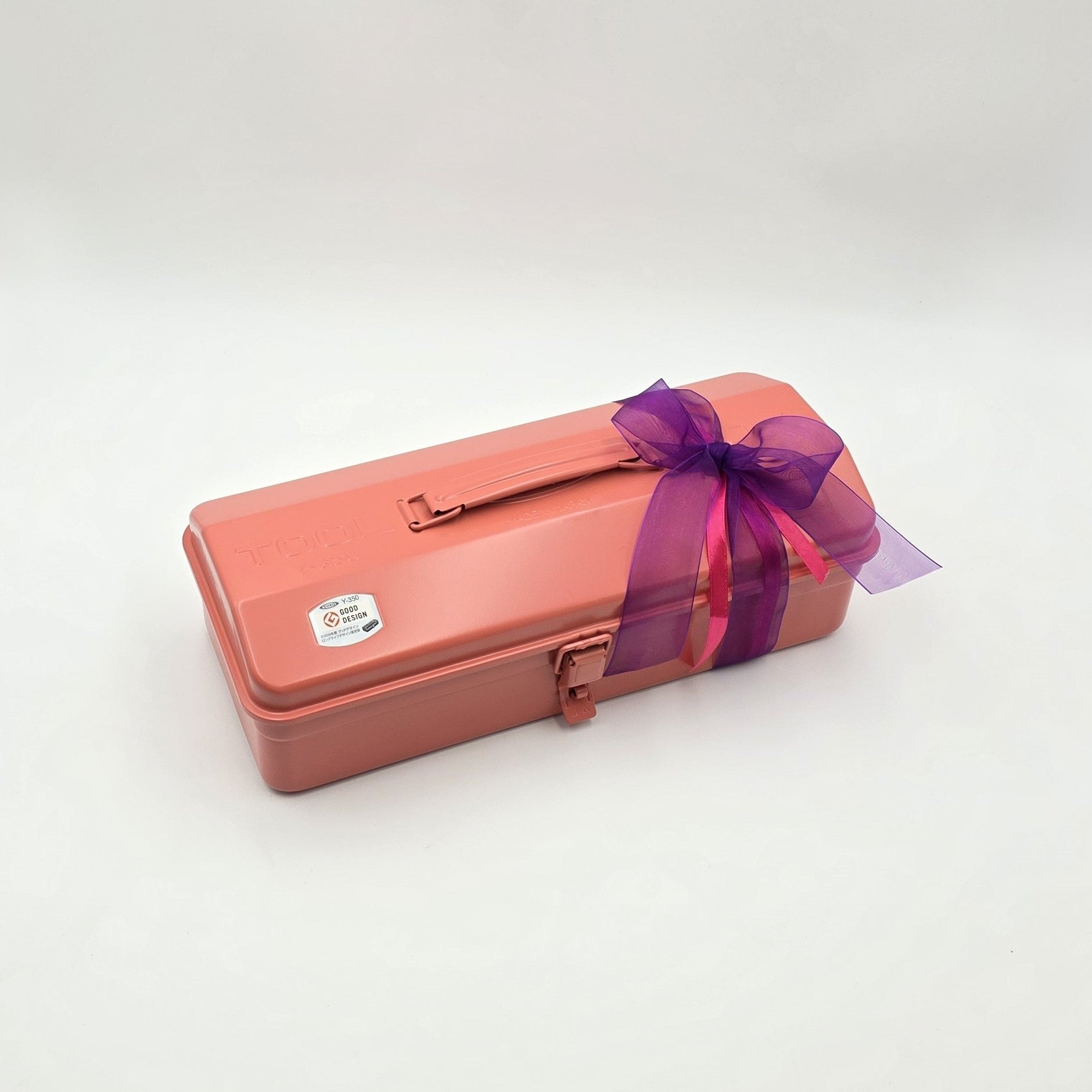 Geschlossene coralfarbene Geschenkbox Royal Coral mit violetter Schleife.